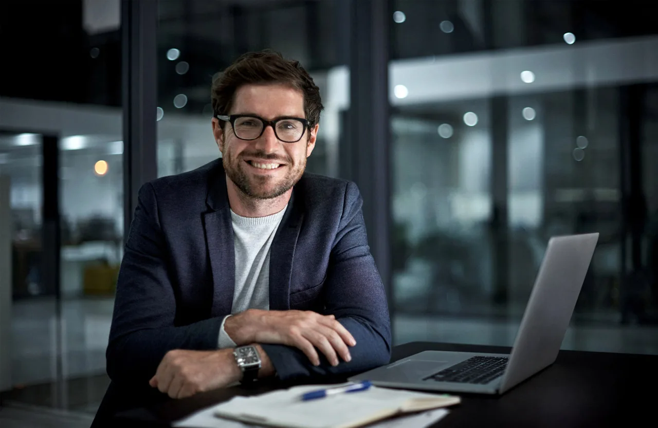 empresario sonriendo en un despacho con el ordenador y unos informes delante